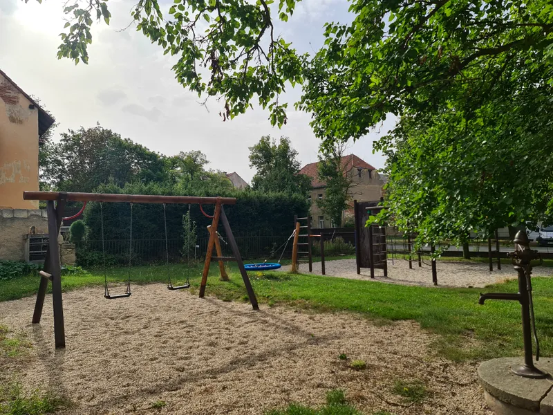 Školní zahrada s&nbsp;houpačkami, prolézačkami a&nbsp;travnatou plochou pod stromy